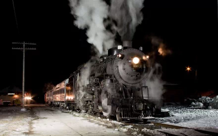 HD desktop wallpaper of a vintage steam train emitting smoke at a nighttime station, showcasing the vehicle's powerful headlight and detailed engine.