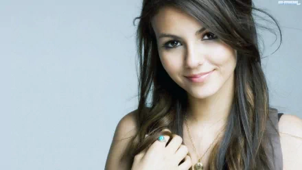 A high-definition desktop wallpaper featuring celebrity Victoria Justice, showcasing her friendly smile and long, wavy hair against a soft gray background.