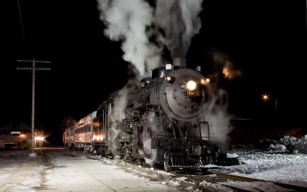 HD desktop wallpaper of a vintage steam train emitting smoke at a nighttime station, showcasing the vehicle's powerful headlight and detailed engine.