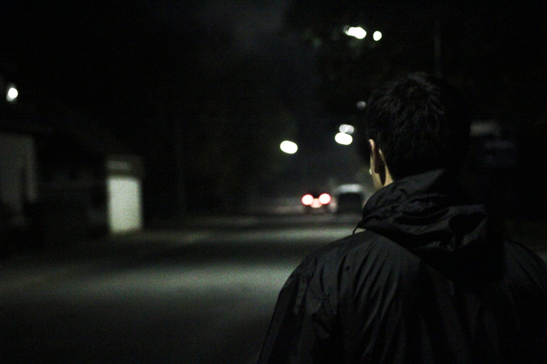 A dark photography scene features a person walking down a dimly lit street, captured in 4K Ultra HD, creating a moody atmosphere for a desktop wallpaper.