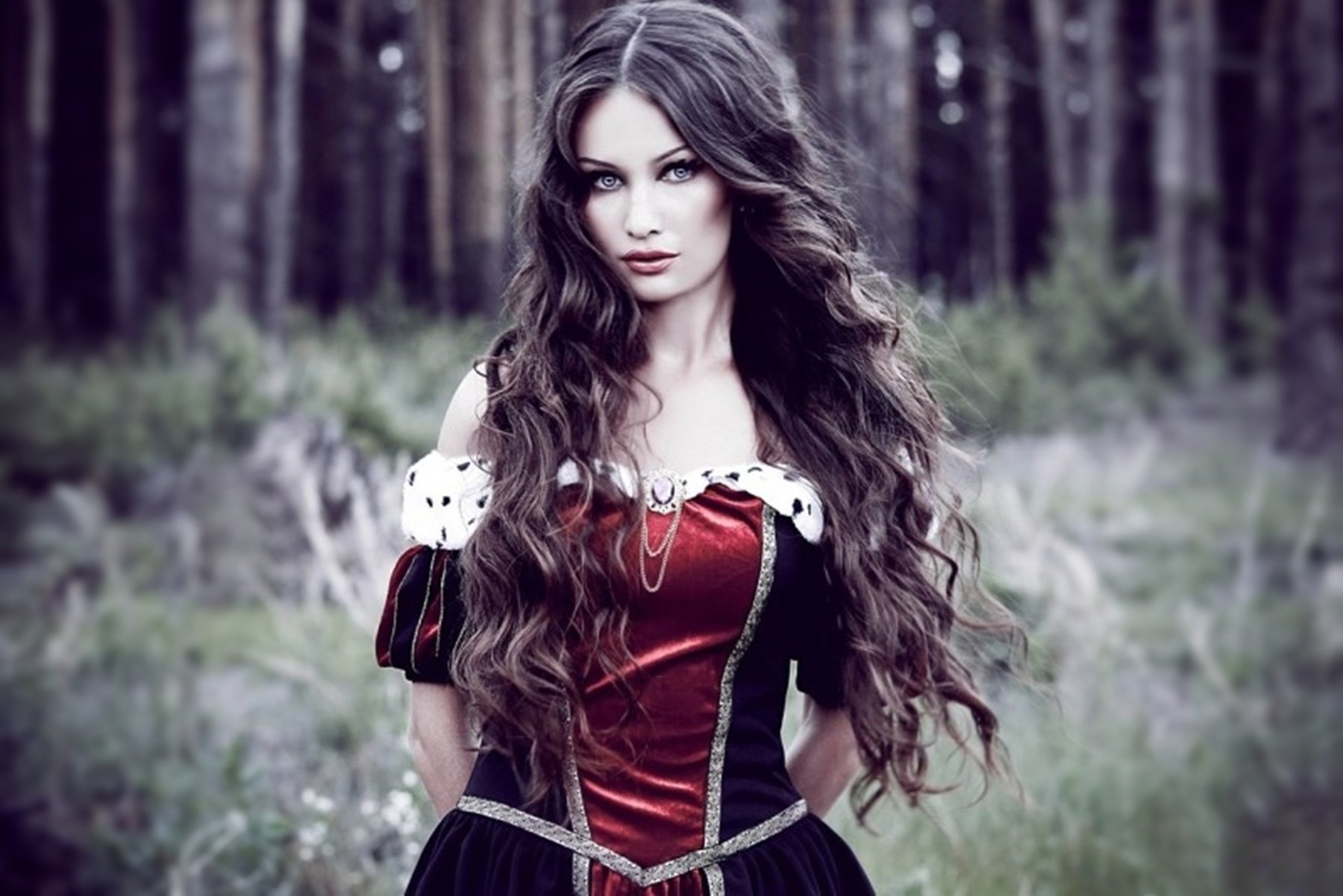 A model in a vintage-inspired red and black dress stands against a lush forest backdrop, showcasing elegance and confidence. This striking image makes for an impressive HD desktop wallpaper.