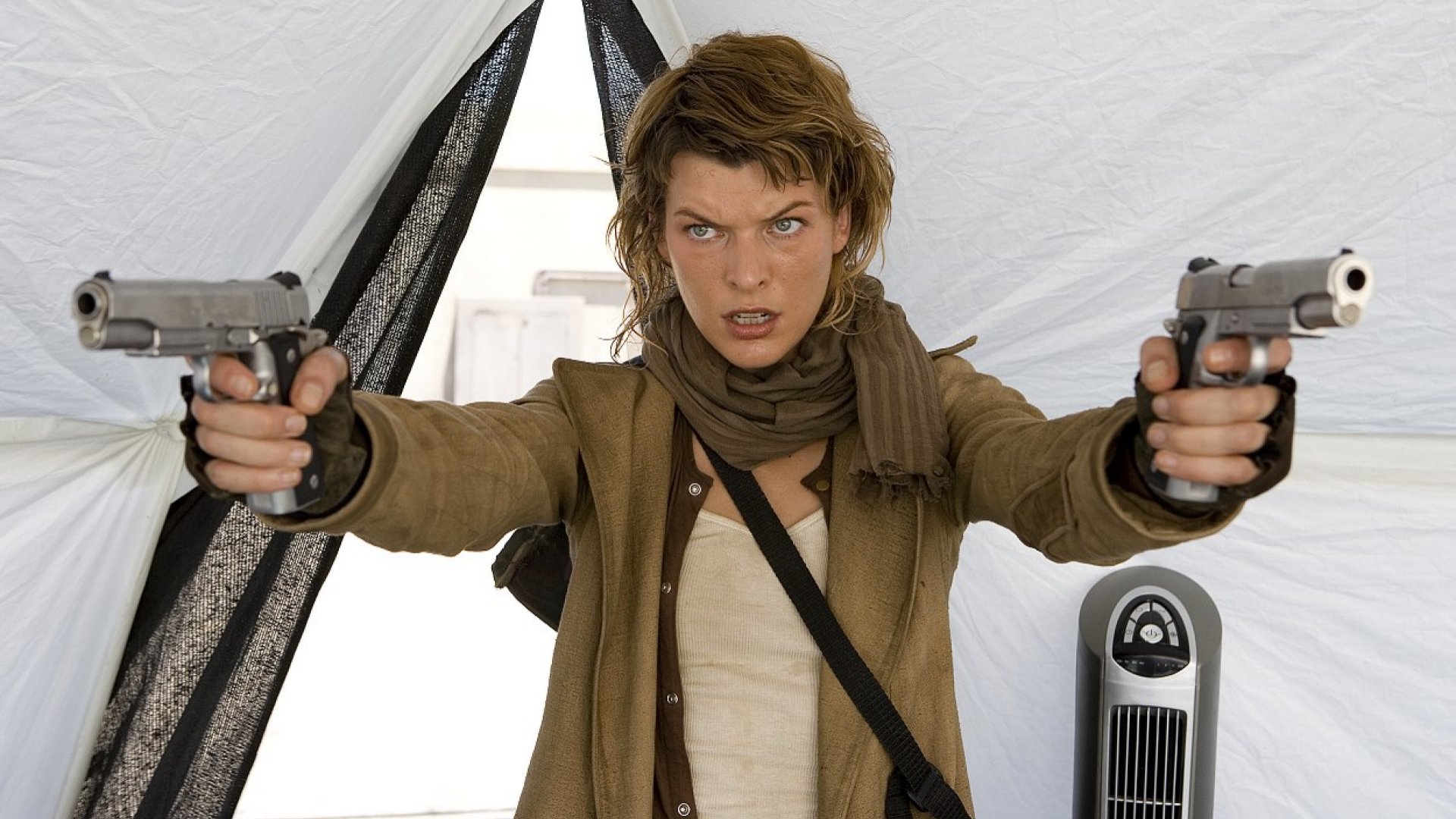 A character from Resident Evil: Extinction stands in a tent, holding two guns with an intense expression, ready for action. This HD PC desktop wallpaper captures the film's thrilling atmosphere.