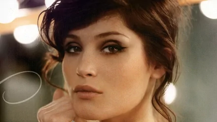 Gemma Arterton poses elegantly, showcasing her striking features against a backdrop of soft lights. This image serves as a captivating HD desktop wallpaper.