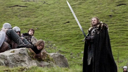A dramatic scene from Game of Thrones featuring Eddard Stark (Sean Bean) confronting Theon Greyjoy (Alfie Allen) amid a tense standoff, set against a lush green landscape.