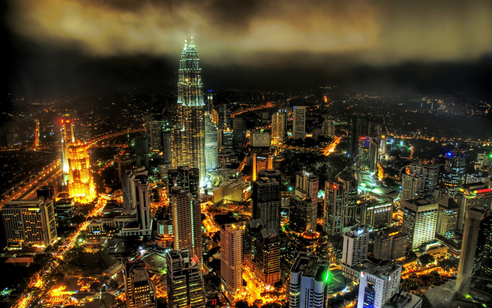 Nighttime aerial view of Kuala Lumpur featuring the illuminated Petronas Towers, showcasing the vibrant man-made skyline of Malaysia in HD quality.