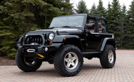 HD desktop wallpaper featuring a rugged black Jeep with large off-road tires, parked on a brick surface, set against a backdrop of trees.
