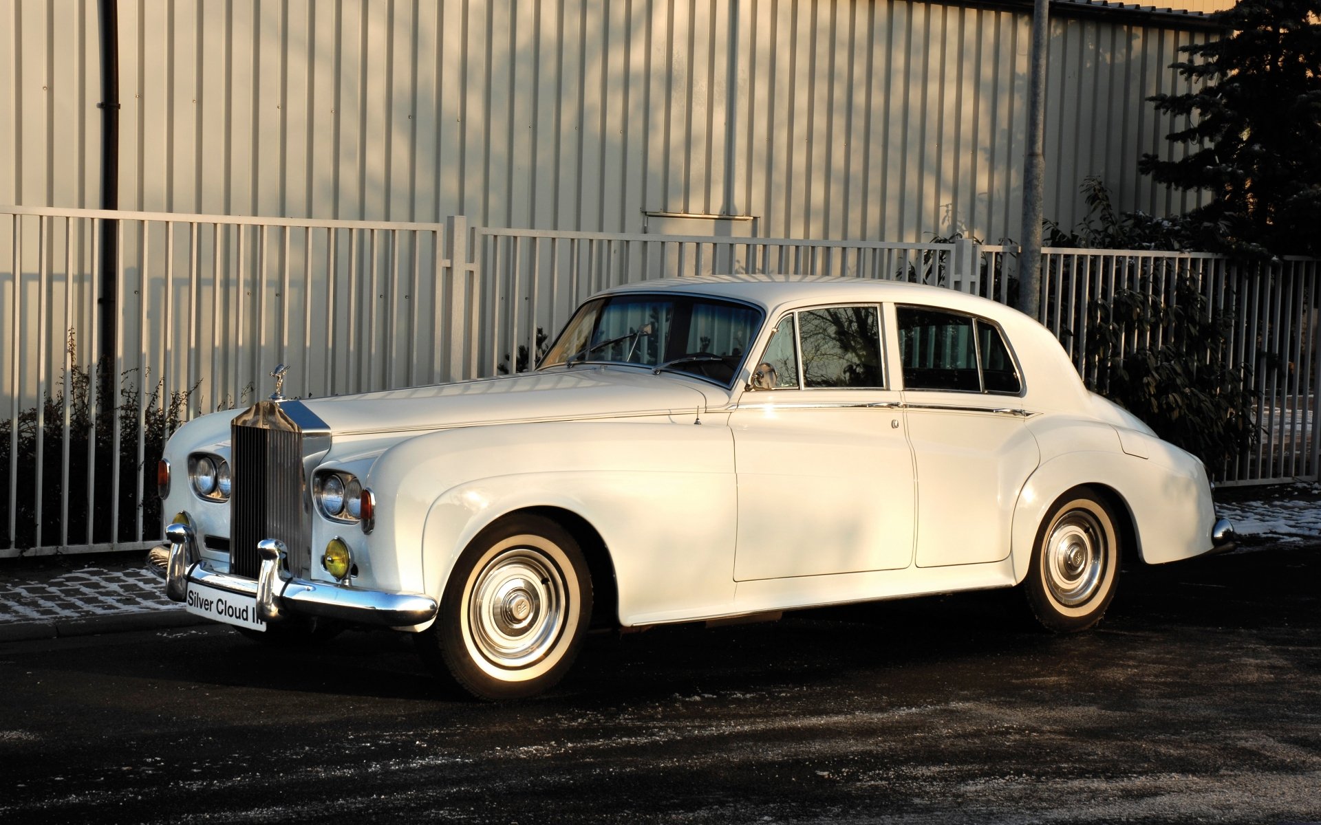 HD desktop wallpaper featuring a classic white Rolls-Royce parked on a street with a metal fence and building in the background.