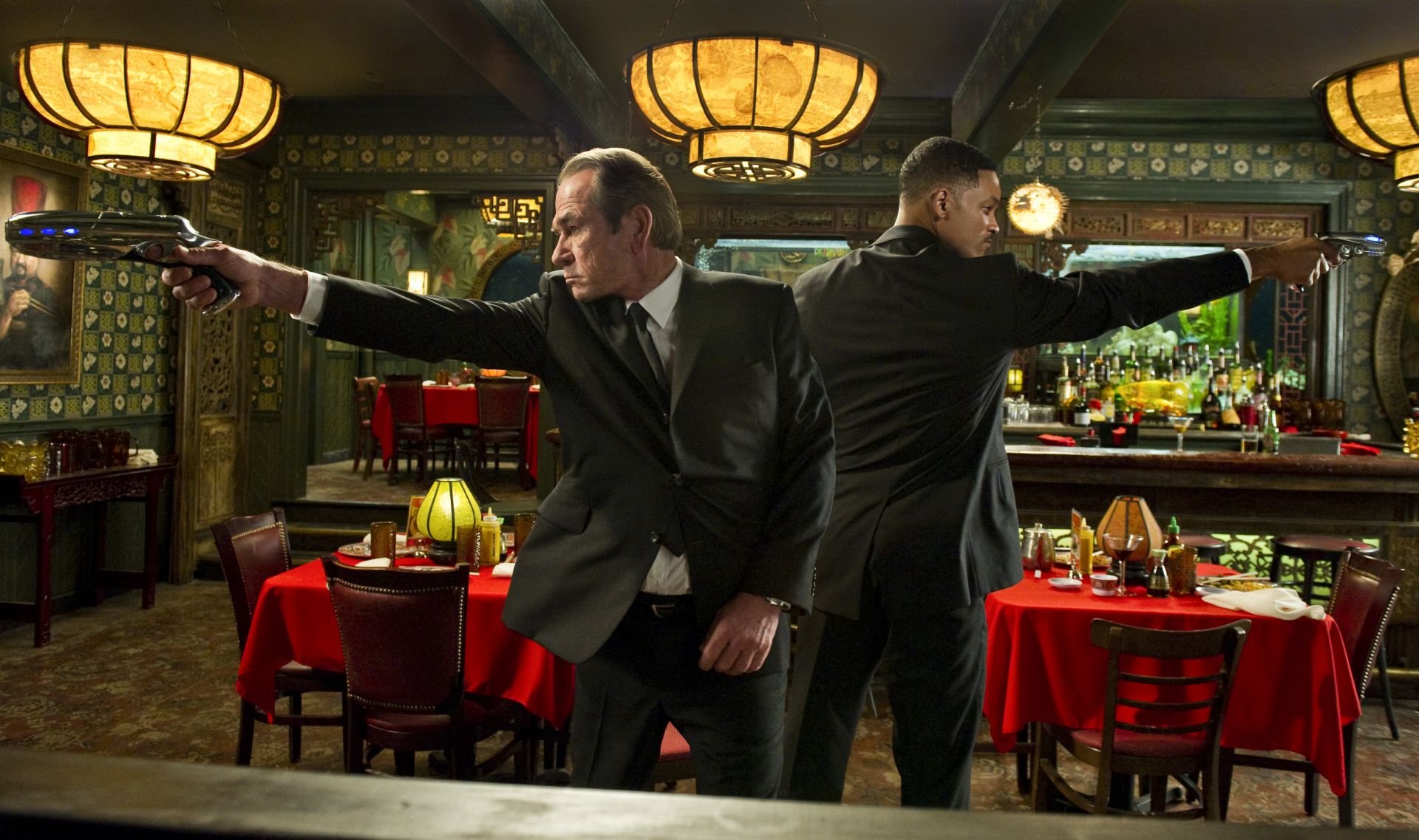 HD PC desktop wallpaper featuring a scene from the movie Men In Black 3 with two agents in black suits aiming guns inside a retro-styled restaurant.