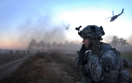 HD PC desktop wallpaper: U.S. Army infantry soldier with weapon and radio, gun at ready in a dusty war zone, helicopters rising over the horizon.