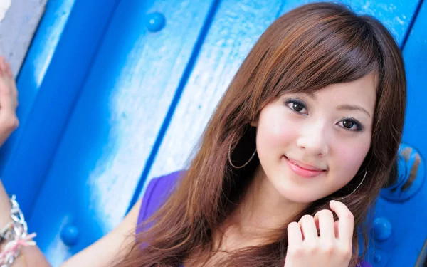 HD wallpaper featuring an oriental Asian woman, Mikako Zhang Kaijie, posing against a vibrant blue background, exuding confidence and elegance.