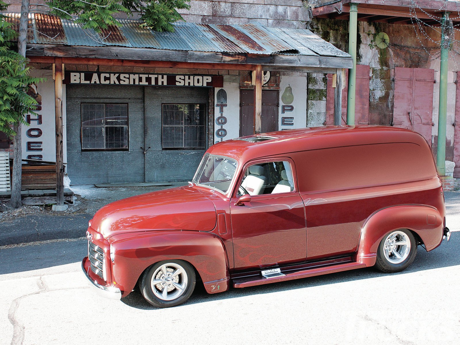 HD PC desktop wallpaper/background: glossy red vintage GMC panel van parked before a rustic Blacksmith Shop.