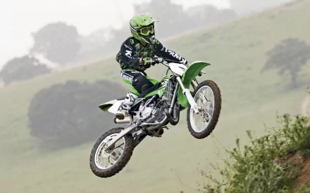 HD desktop wallpaper featuring a motocross rider in mid-air jump, surrounded by a natural landscape backdrop. Tags: motocross, sports.