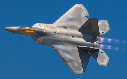 A Lockheed Martin F-22 Raptor jet soars against a clear blue sky, showcasing its impressive design and agility. This vibrant HD wallpaper captures the essence of military aviation.
