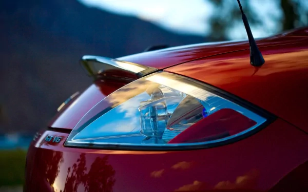Close-up of a red Mitsubishi Eclipse Spyder vehicle front headlight and hood with small spoiler, glossy finish against a blurred mountain backdrop — HD PC desktop wallpaper background.
