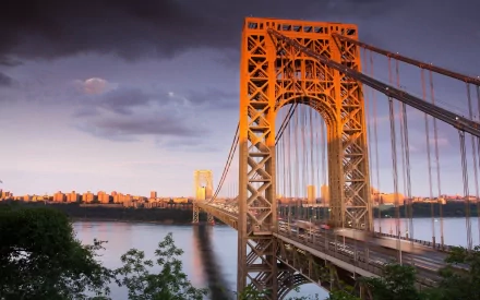 2K Quad HD PC desktop wallpaper of the George Washington Bridge in New York — a man-made steel suspension bridge over the Hudson at sunset with a distant skyline.