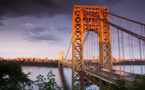 2K Quad HD PC desktop wallpaper of the George Washington Bridge in New York — a man-made steel suspension bridge over the Hudson at sunset with a distant skyline.