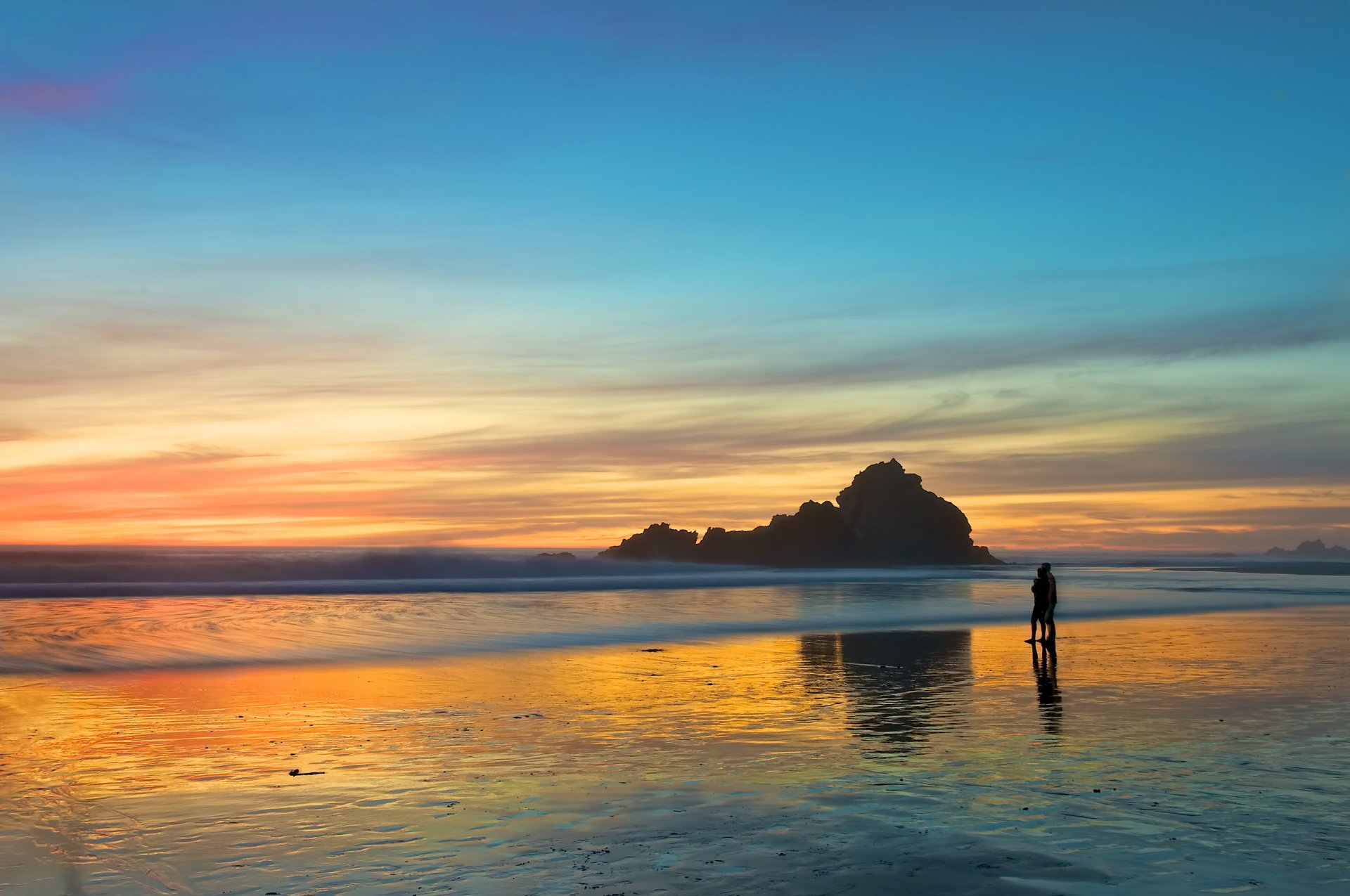 HD desktop wallpaper photography of a person standing on a reflective wet beach during a vibrant sunset with clouds and calm ocean waters.