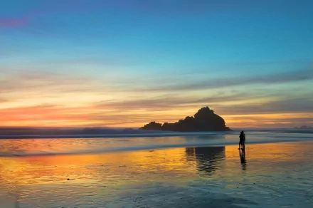 HD desktop wallpaper photography of a person standing on a reflective wet beach during a vibrant sunset with clouds and calm ocean waters.