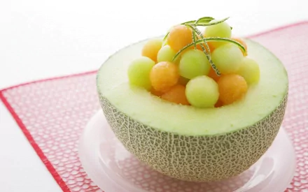 HD desktop wallpaper featuring a halved melon filled with green and orange melon balls on a white plate over a red placemat.