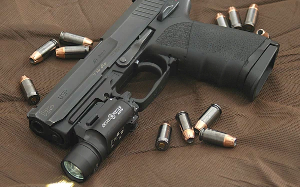HD desktop wallpaper featuring a man-made Heckler & Koch pistol surrounded by scattered bullets on a textured fabric background.
