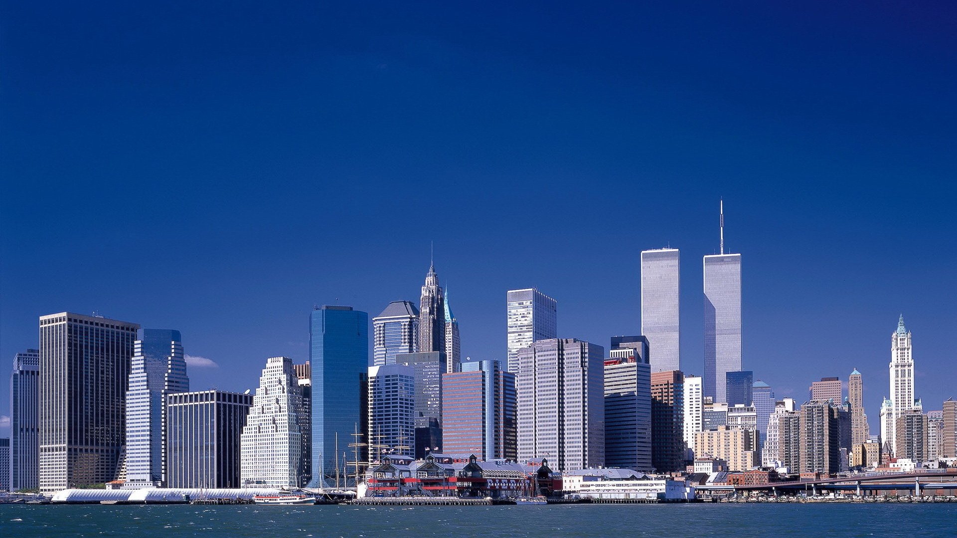 HD desktop wallpaper showcasing the iconic Manhattan skyline in New York with its famous man-made skyscrapers under a clear blue sky.