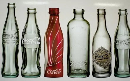 HD PC desktop wallpaper showing a lineup of six man-made Coca-Cola bottles in various vintage and modern designs against a white background.