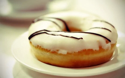 HD desktop wallpaper featuring a close-up of a doughnut with white icing and chocolate drizzle on a white plate.