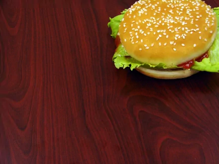 A close-up of a delicious hamburger with sesame seeds, lettuce, and ketchup, set against a rich wooden background, creating an appetizing HD desktop wallpaper.