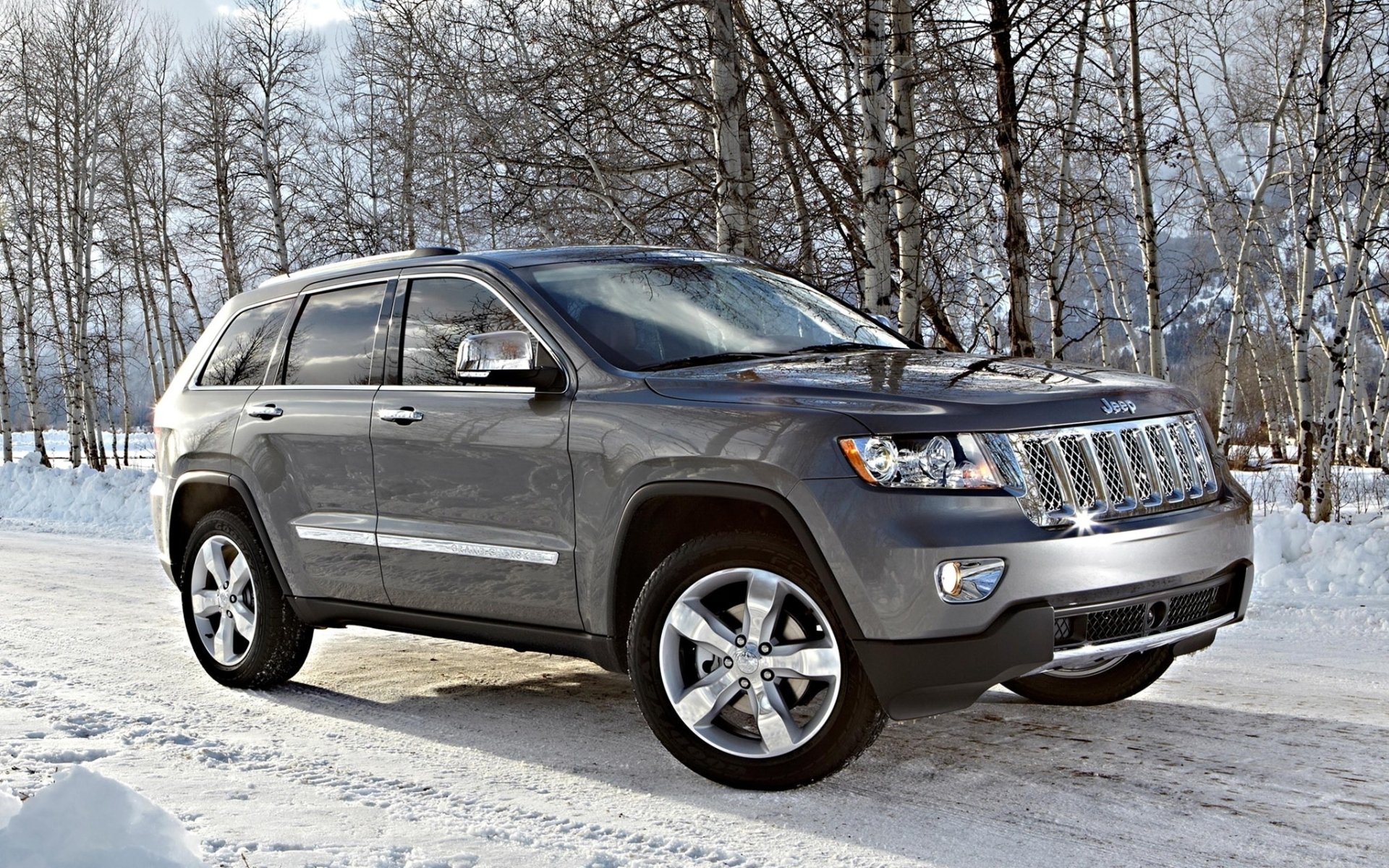 HD PC desktop wallpaper of a gray Jeep SUV parked on a snow-covered road with leafless trees and distant mountains as the background