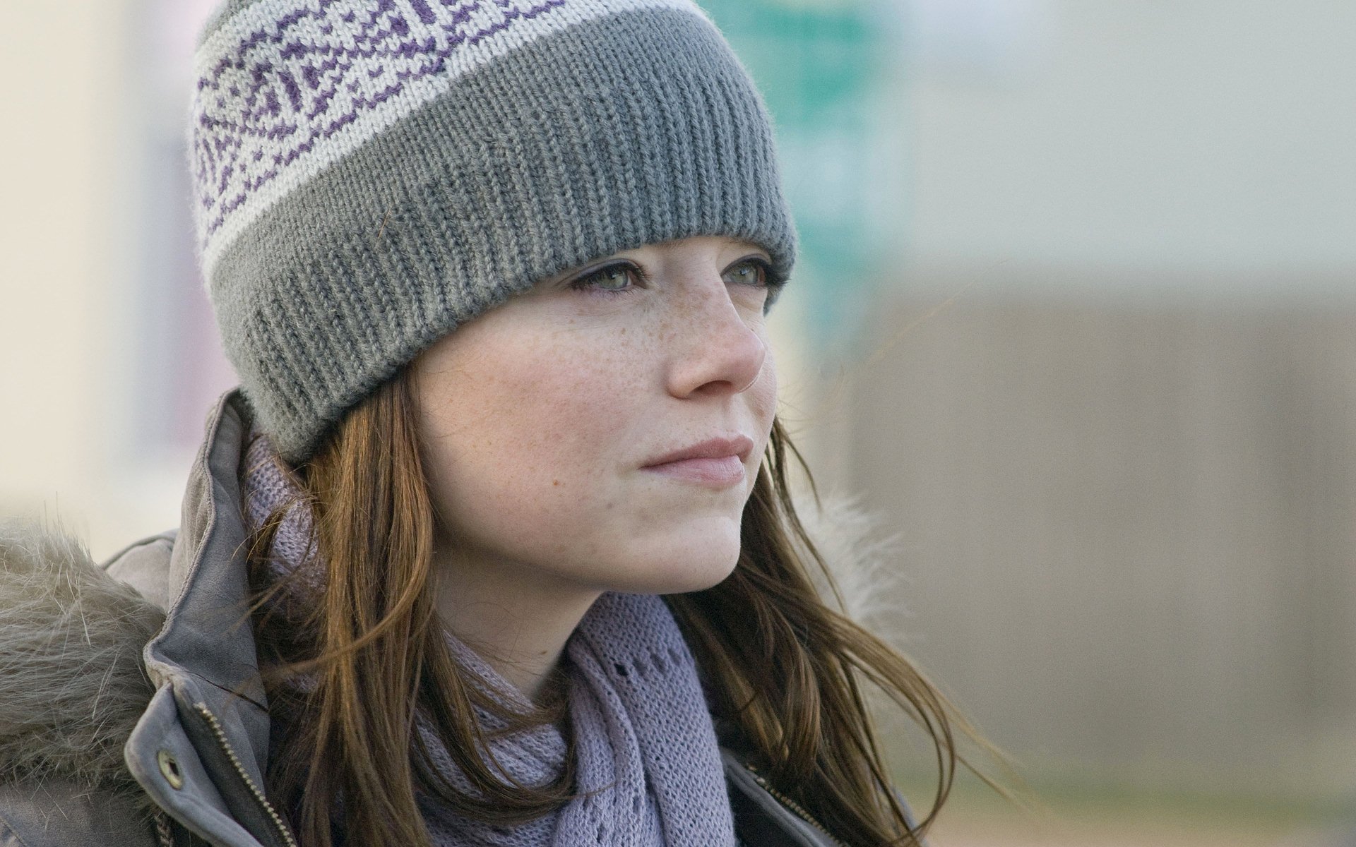 Emma Stone gazes thoughtfully in a cozy gray knit hat and jacket, captured in this HD desktop wallpaper. A serene moment showcasing her natural beauty.