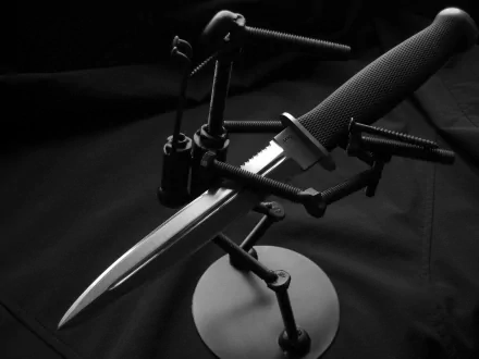 A close-up image of a sharp knife, artistically displayed with black background and metal stands, serves as a striking HD PC desktop wallpaper and background.