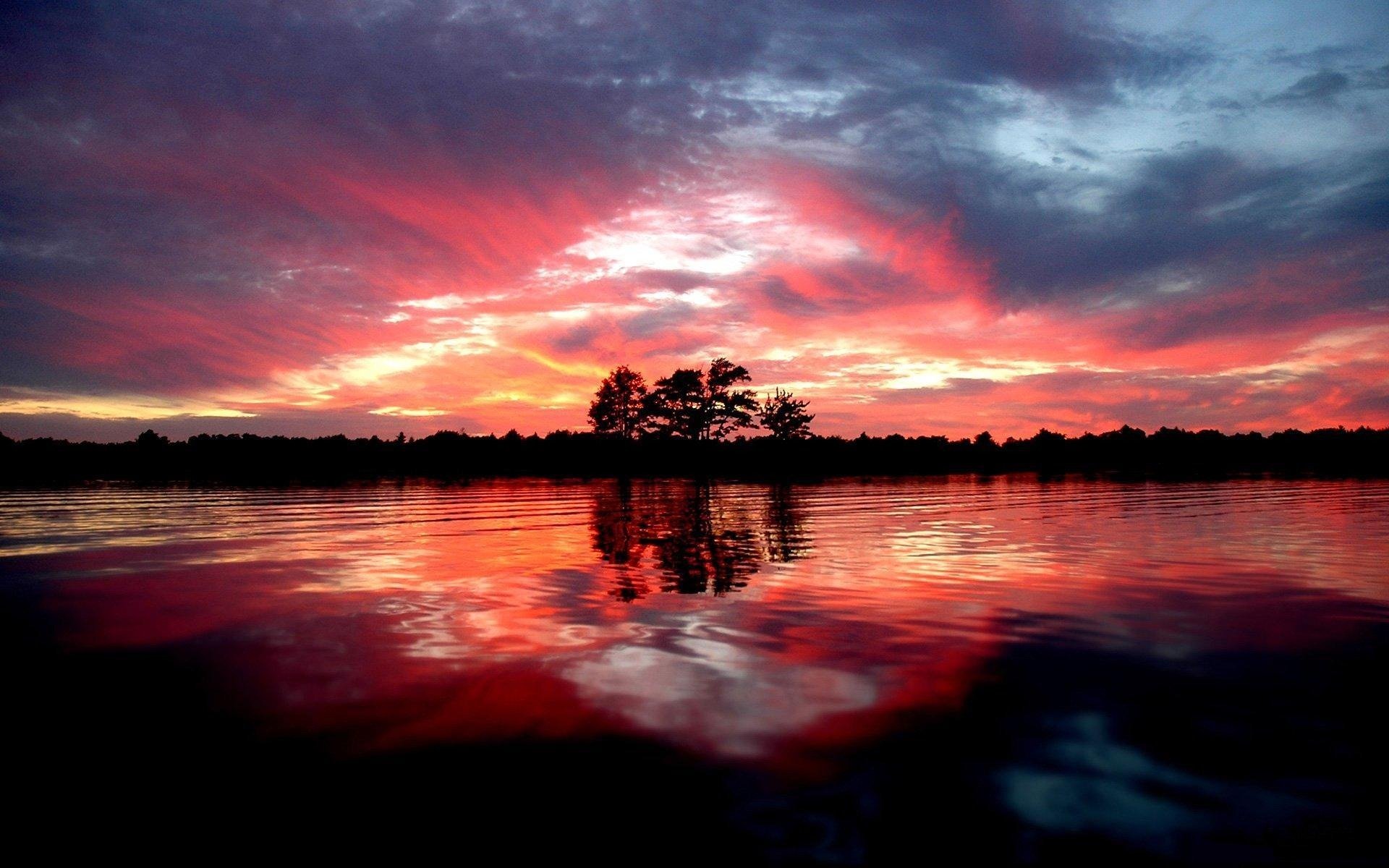 HD PC desktop wallpaper of a scenic nature view featuring a fiery sunset sky reflected on a calm lake with silhouetted trees on the horizon.