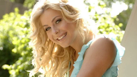 Julianne Hough beams playfully in a vibrant outdoor setting, showcasing her blonde curls and radiant smile. This HD wallpaper captures her charismatic presence effortlessly.