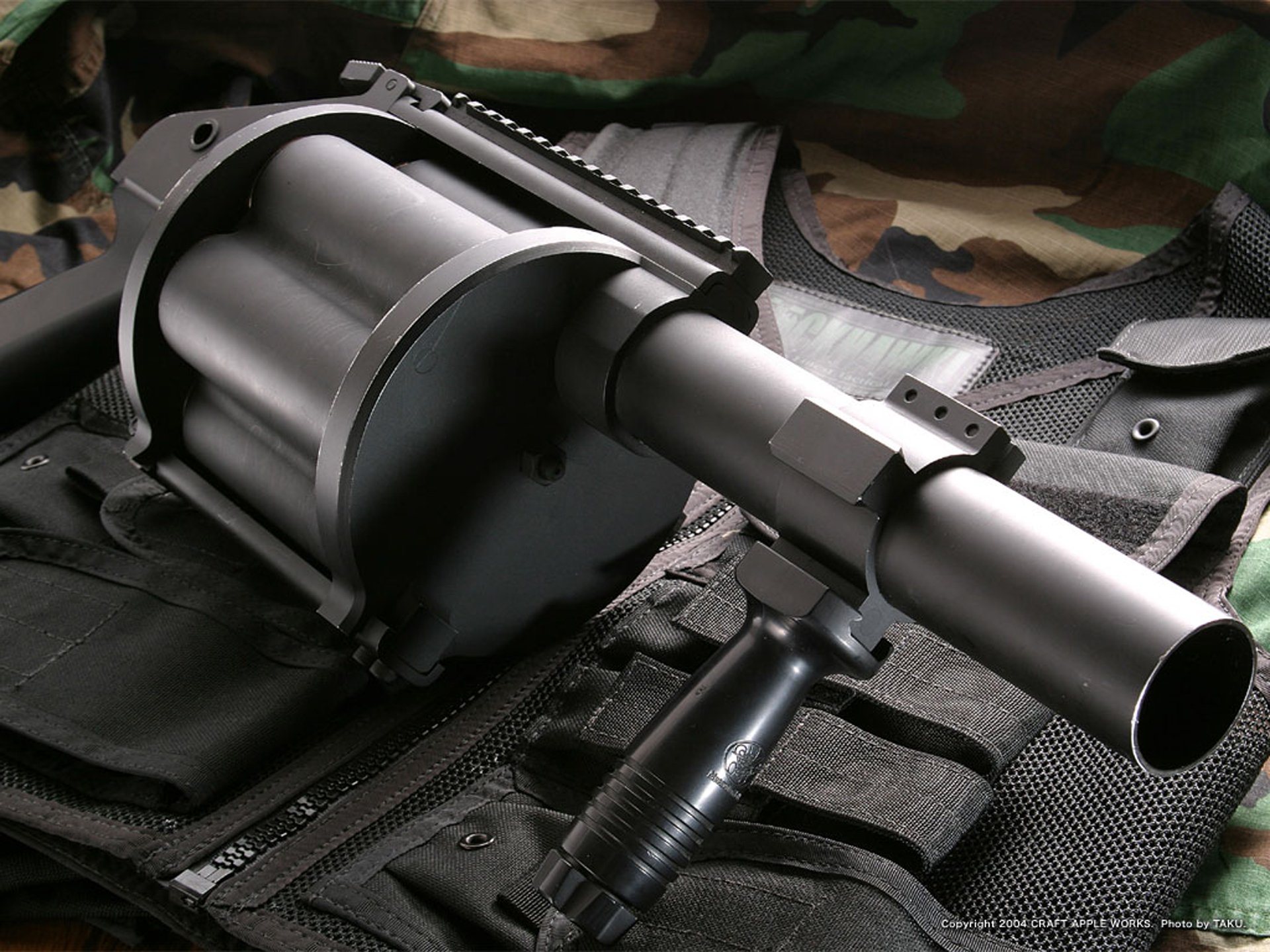 HD PC desktop wallpaper: close-up of a military rocket launcher on a tactical vest, matte metal barrel and revolving cylinder in sharp focus against a subdued camouflage background.