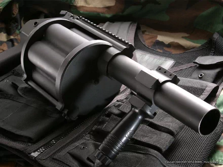 HD PC desktop wallpaper: close-up of a military rocket launcher on a tactical vest, matte metal barrel and revolving cylinder in sharp focus against a subdued camouflage background.