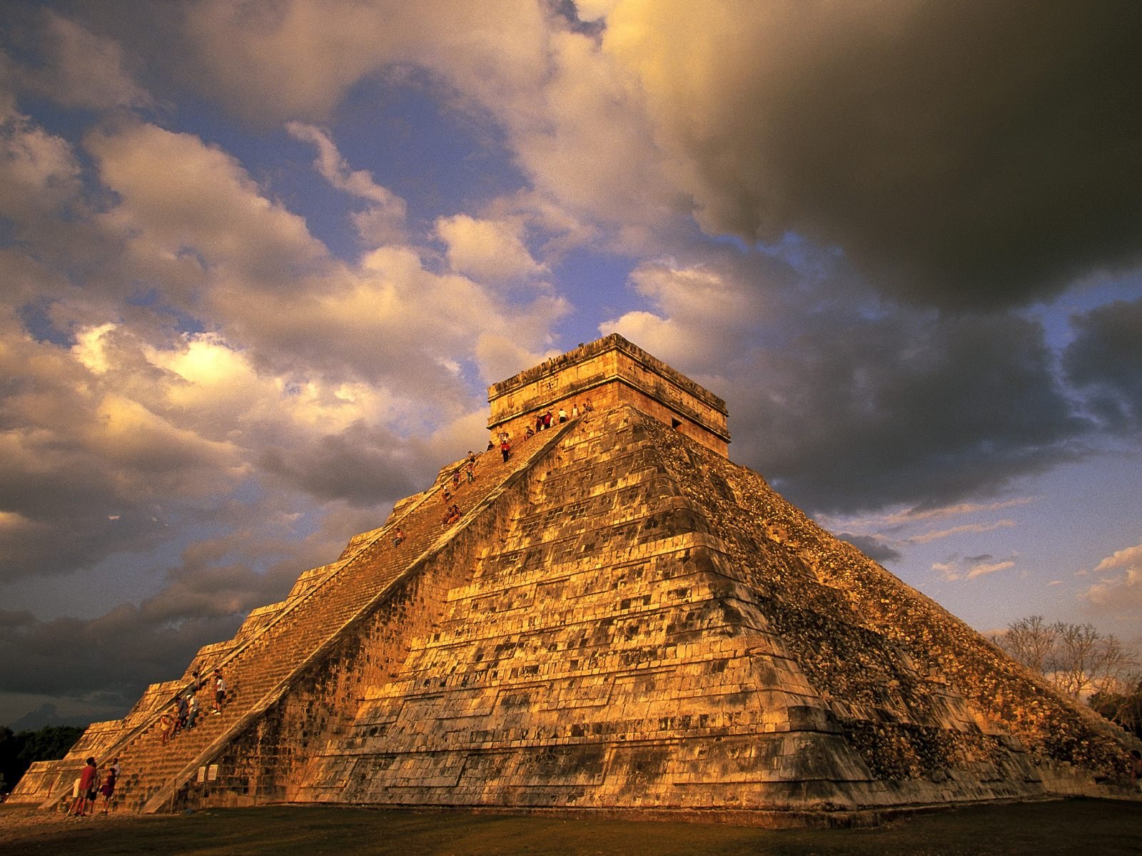 HD desktop wallpaper showcasing the man-made Chichen Itza pyramid under a dramatic, partly cloudy sky at sunset.