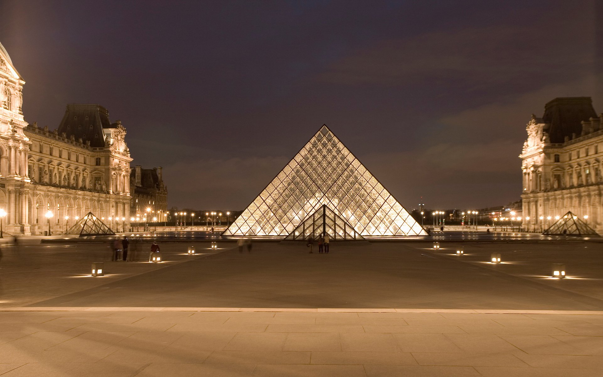 Night view of the illuminated Louvre Pyramid in Paris, showcasing the iconic man-made glass structure with historic buildings in the background as an HD desktop wallpaper.