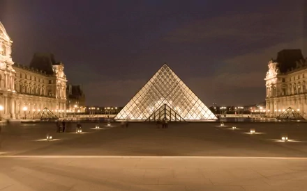 Night view of the illuminated Louvre Pyramid in Paris, showcasing the iconic man-made glass structure with historic buildings in the background as an HD desktop wallpaper.