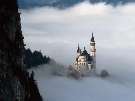 A stunning HD wallpaper of Neuschwanstein Castle partially shrouded in fog, showcasing its enchanting architecture amidst a mystical landscape.