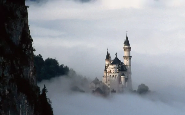 A stunning HD wallpaper of Neuschwanstein Castle partially shrouded in fog, showcasing its enchanting architecture amidst a mystical landscape.