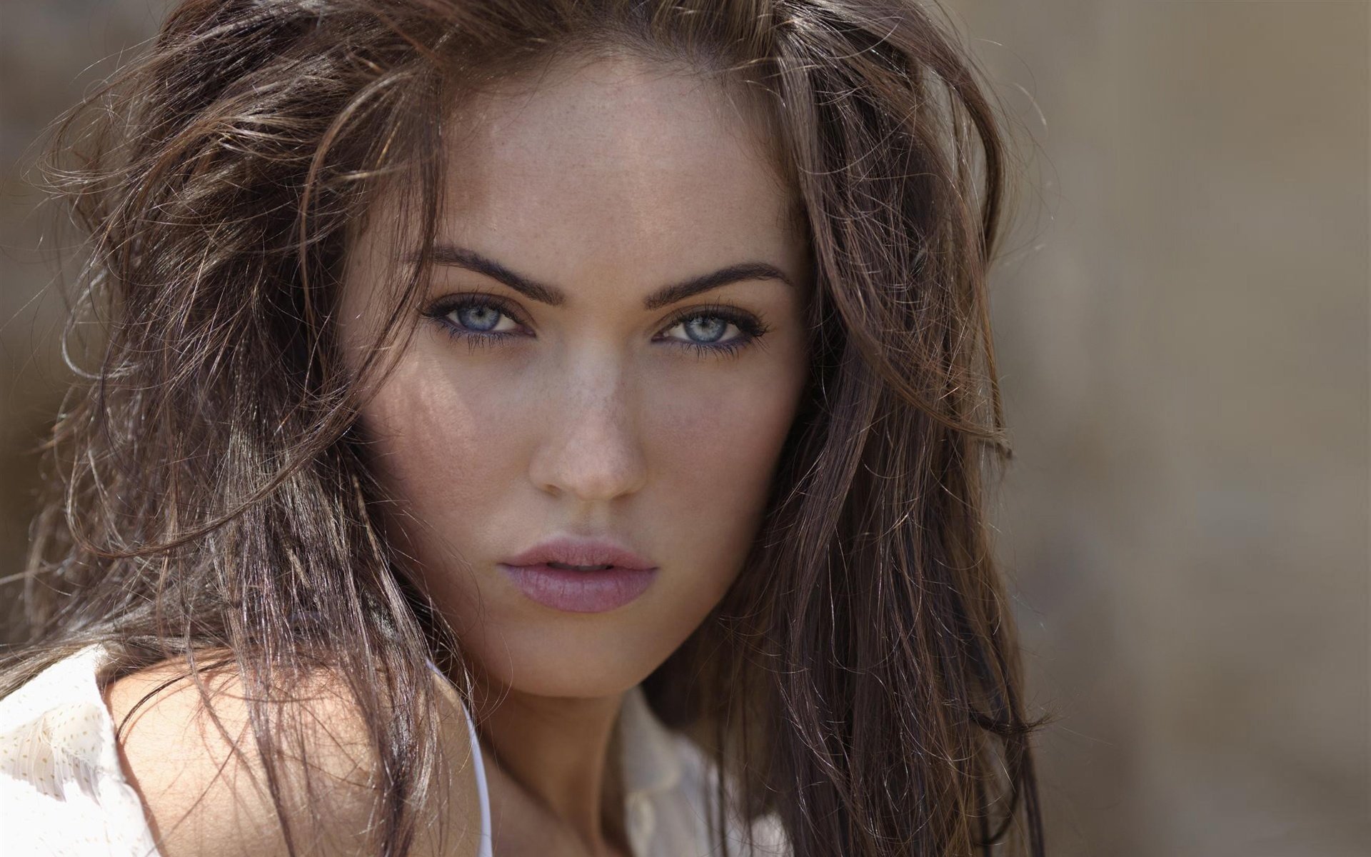A striking close-up of celebrity Megan Fox, featuring her expressive blue eyes and tousled hair. This image serves as an HD desktop wallpaper and background.