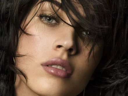 Close-up of actress Megan Fox with tousled dark hair and striking eyes, showcasing her captivating beauty. This image serves as a high-definition desktop wallpaper.