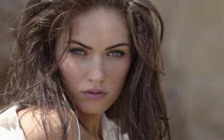 A striking close-up of celebrity Megan Fox, featuring her expressive blue eyes and tousled hair. This image serves as an HD desktop wallpaper and background.