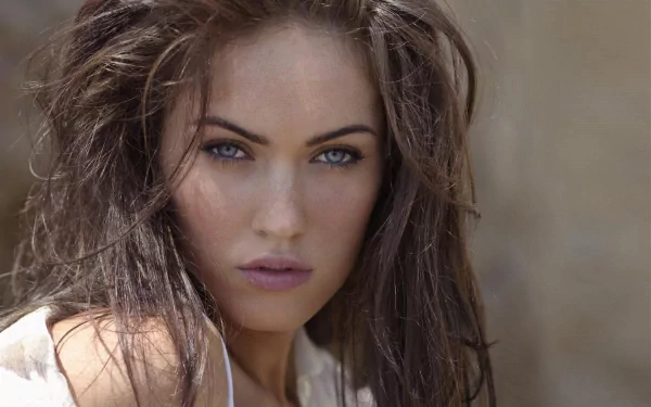 A striking close-up of celebrity Megan Fox, featuring her expressive blue eyes and tousled hair. This image serves as an HD desktop wallpaper and background.