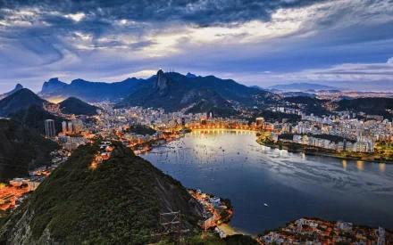 A stunning night view of Rio de Janeiro, Brazil, showcasing the city's architecture and lights from a high vantage point, with vibrant cityscape around a bay, set against a dramatic evening sky.