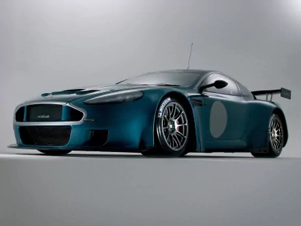 HD desktop wallpaper featuring a sleek Aston Martin DBR9 race car in a dark metallic blue finish, showcased against a simple gray background.