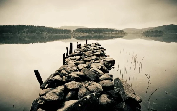 HD desktop wallpaper of an old man-made pier extending into a calm sea under a cloudy sky, surrounded by misty hills in the background.