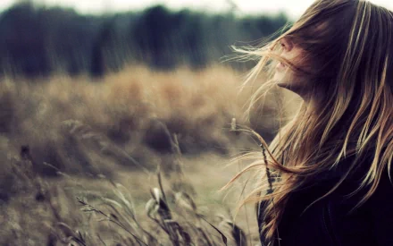 A serene woman with flowing hair gazes into the distance, surrounded by tall grasses, creating a captivating HD desktop wallpaper and background.