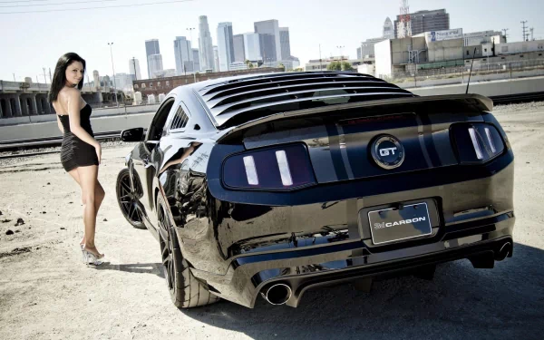 HD PC desktop wallpaper featuring a sleek black Ford GT parked near an urban waterfront with a city skyline in the background and a woman standing beside the car.