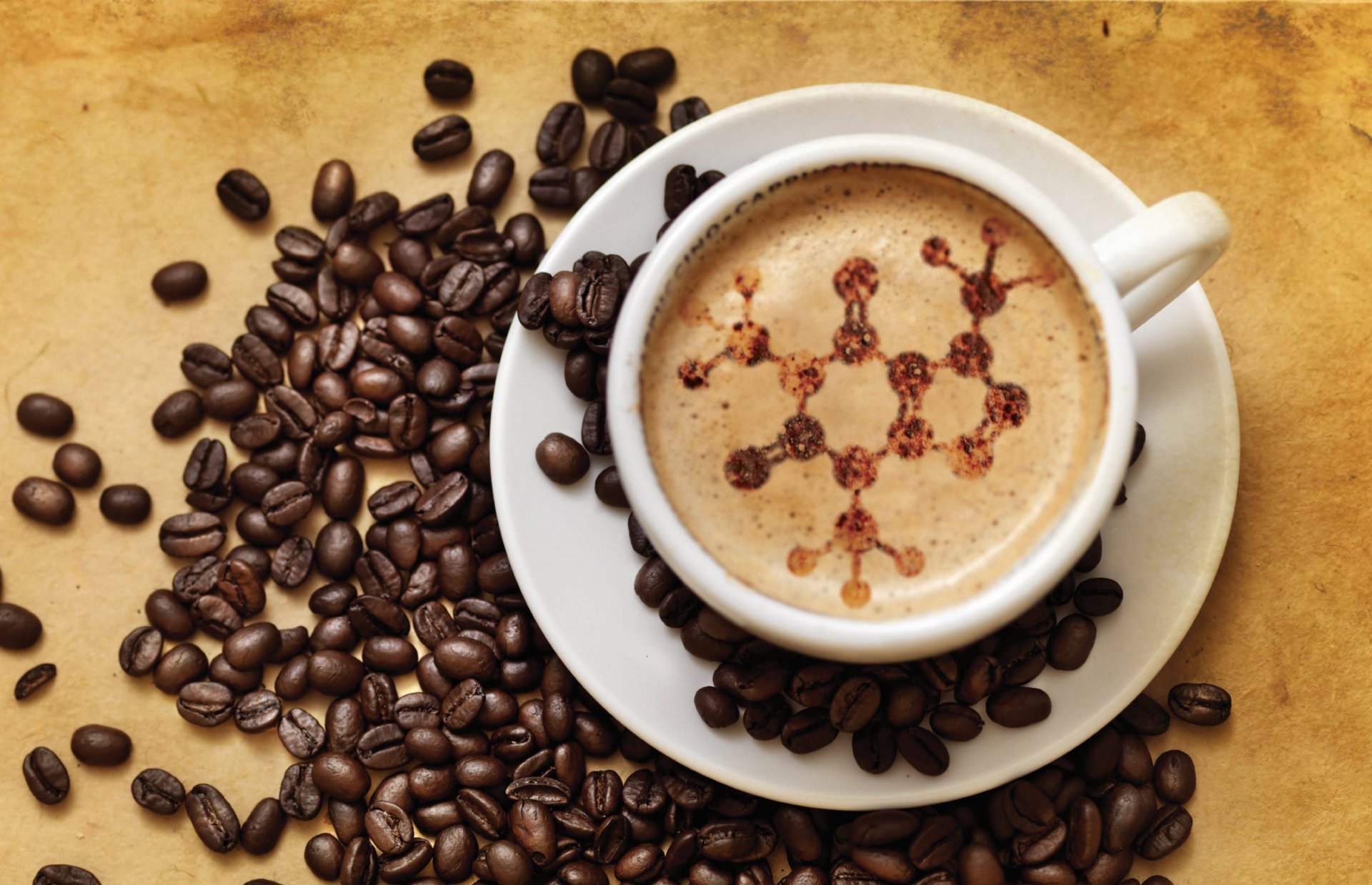 HD desktop wallpaper featuring a cup of coffee with latte art depicting a chemical structure, surrounded by scattered coffee beans on a warm-toned background.